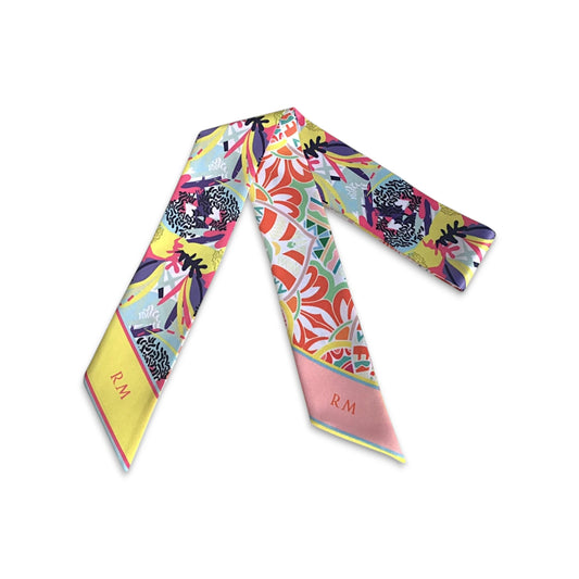 A handbag scarf with a vibrant, multicolor floral and abstract print, featuring a yellow border with an 'R.M.' monogram and a pink border, laid flat on a white background.