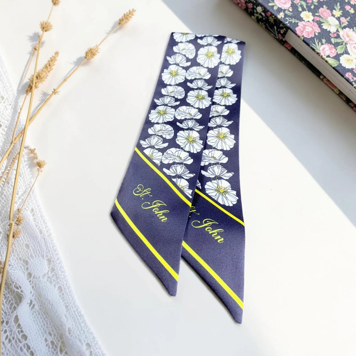 Navy blue skinny scarf decorated with scattered white blossoms, subtle yellow details, and matching personalized pointed tips.