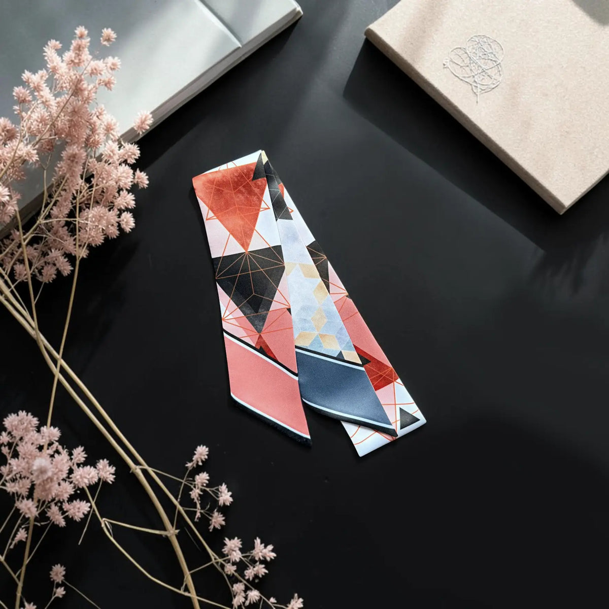 Double-sided satin bag scarf showcasing two coordinated geometric prints, one with coral and black triangles and the other with blue, grey, and beige hexagonal patterns.