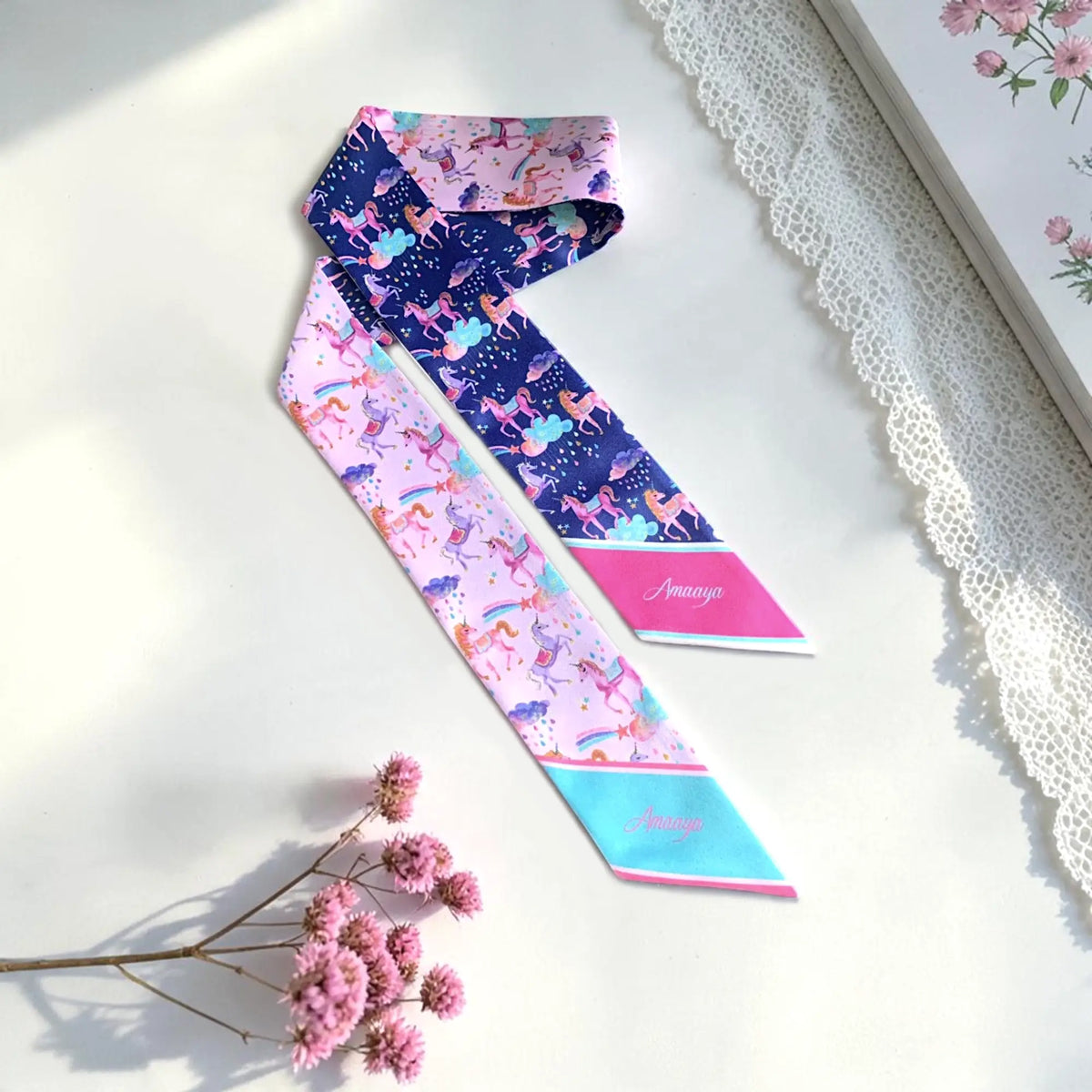 Personalised pink and navy blue unicorn twilly scarves featuring colourful rainbows, fluffy clouds, sparkling stars, and custom name details.