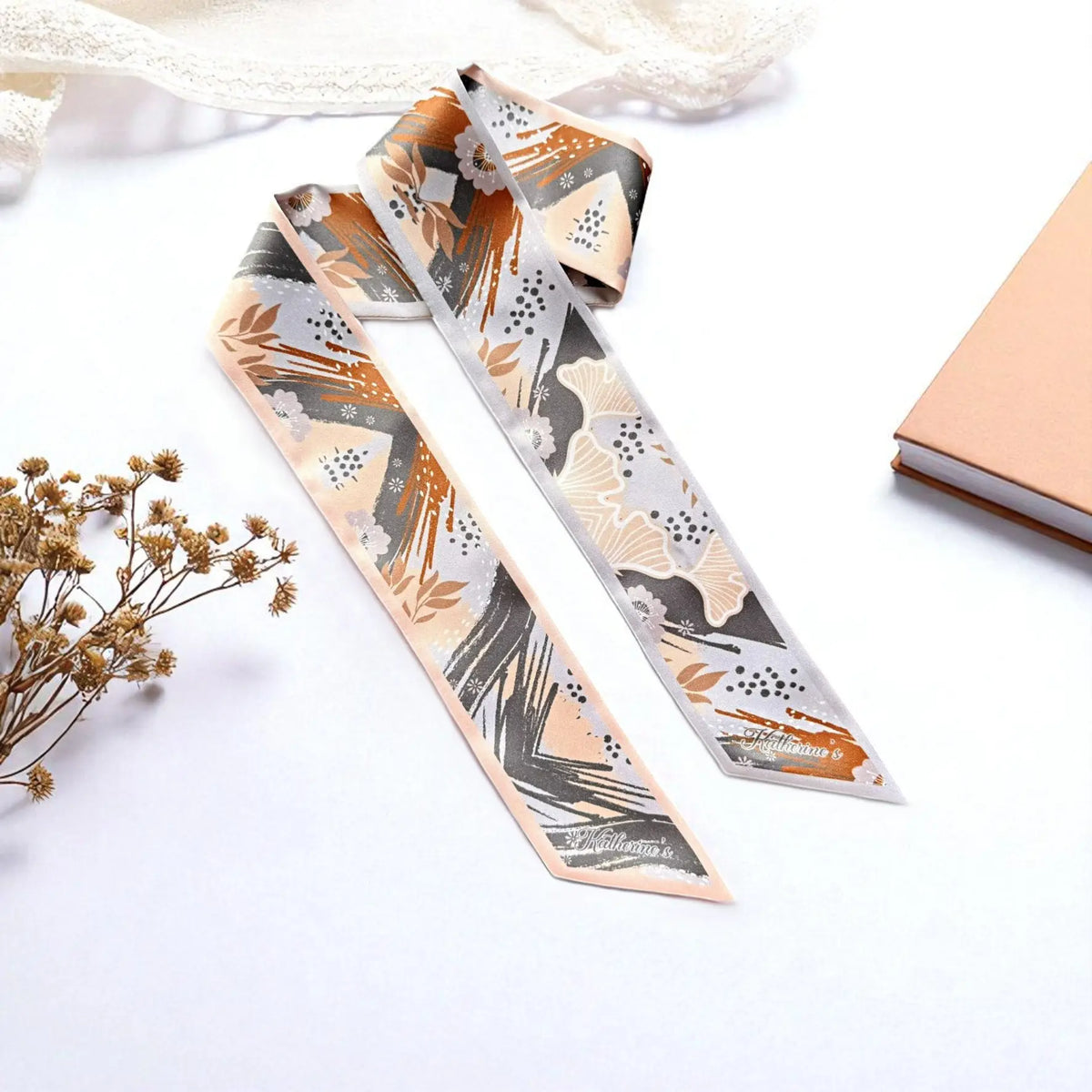 Personalised skinny twilly scarf featuring abstract floral patterns, ginkgo leaves, terracotta brushstrokes, and soft peach and grey tones, styled on a white background.
