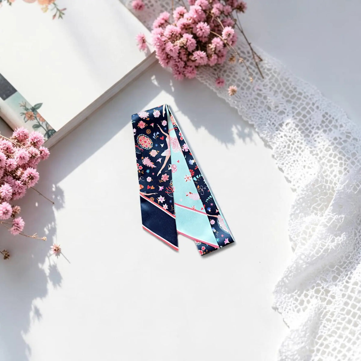 Elegant ballet-themed twilly scarf featuring graceful ballerinas, romantic pink flowers, and whimsical decorative motifs, styled with dried pink flowers and white lace.