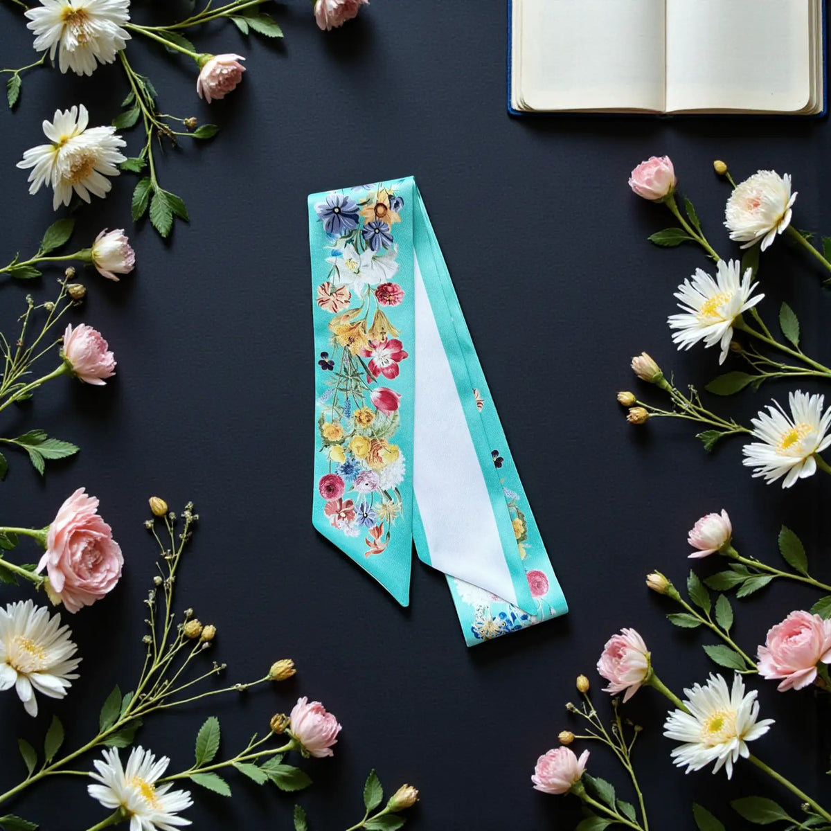 Personalised turquoise floral handbag scarf featuring delicate garden flowers and botanical details, styled with fresh daisies and pink roses.