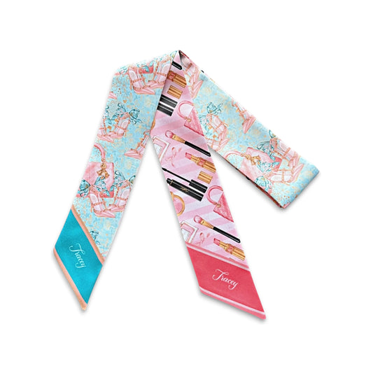 Pink skinny scarf featuring illustrations of lipsticks, makeup brushes, perfume bottles, and handbags, with a personalised name printed on the pointed end.