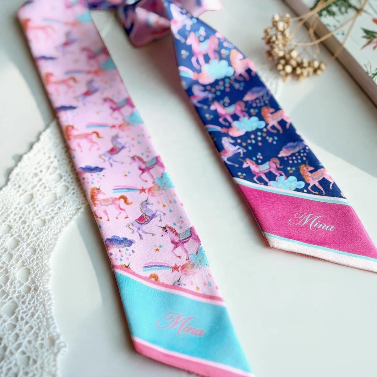 Pastel pink unicorn twilly scarf featuring illustrated unicorns, colourful rainbows, tiny stars, and a turquoise blue tip personalised with a name.