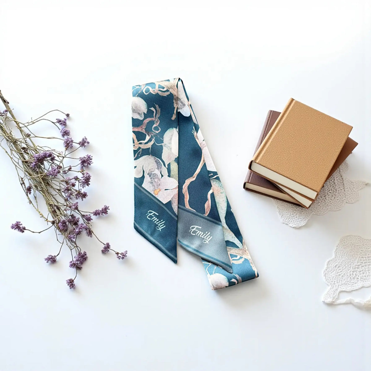 Close-up of a personalized floral scarf featuring the name Emily in white cursive lettering on deep teal and muted gray pointed ends.