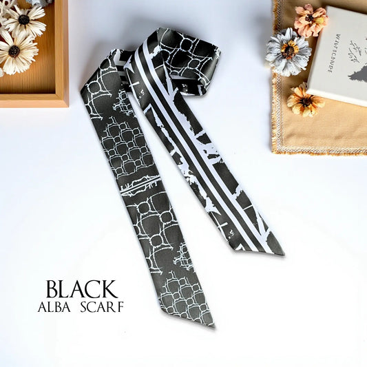 Black skinny twilly scarf featuring a white geometric pattern, contrasting stripes, and abstract motifs, styled with dried flowers and books.