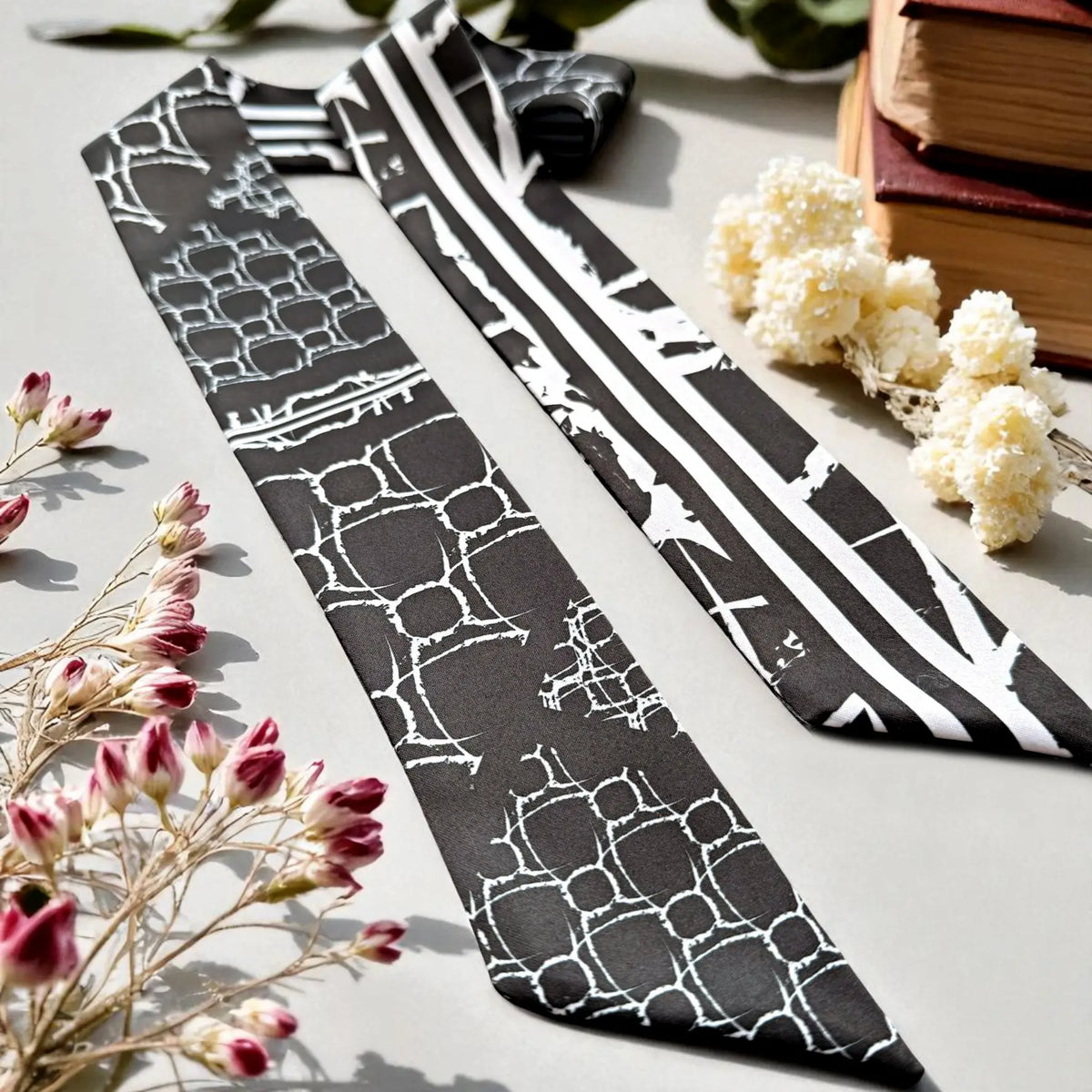 Elegant black and white handbag scarf featuring a geometric design and bold striped pattern, displayed with decorative flowers.
