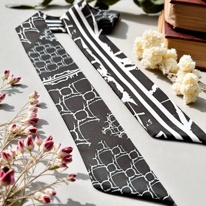 Elegant black and white handbag scarf featuring a geometric design and bold striped pattern, displayed with decorative flowers.