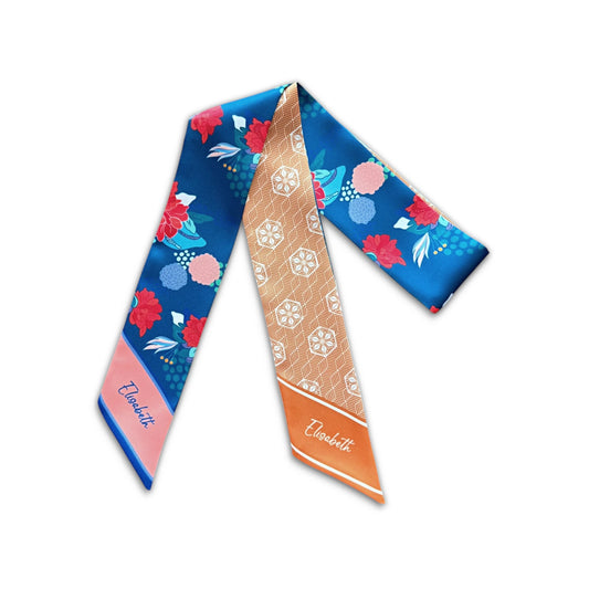 Close-up of a blue satin skinny scarf decorated with colourful flowers, turquoise leaves, and delicate botanical details, finished with a pink pointed end featuring the name Elisabeth.