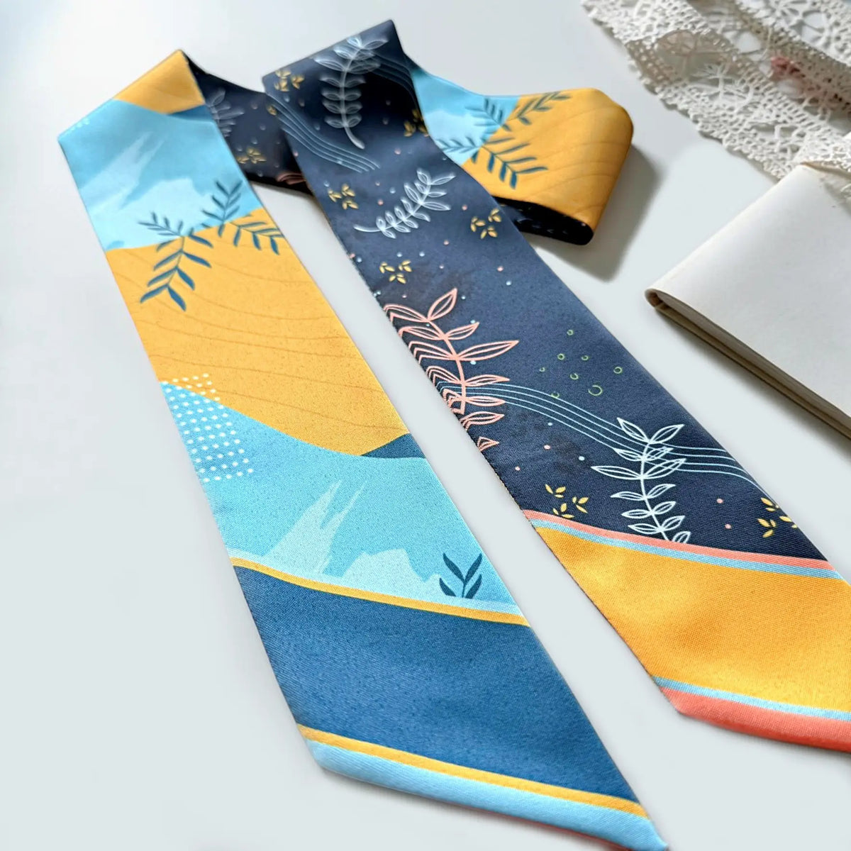 Blue and yellow skinny scarf featuring modern geometric shapes, delicate botanical line drawings, and pointed ends with personalised name details on a white background.