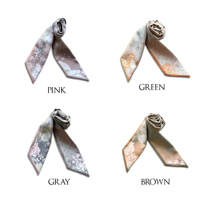 Four silk scarves with floral patterns are displayed in a 2x2 grid with labels 'PINK', 'GREEN', 'GRAY', and 'BROWN' underneath. The scarves feature a delicate watercolor-style floral design in muted tones of pink, green, gray, and brown on a white background.