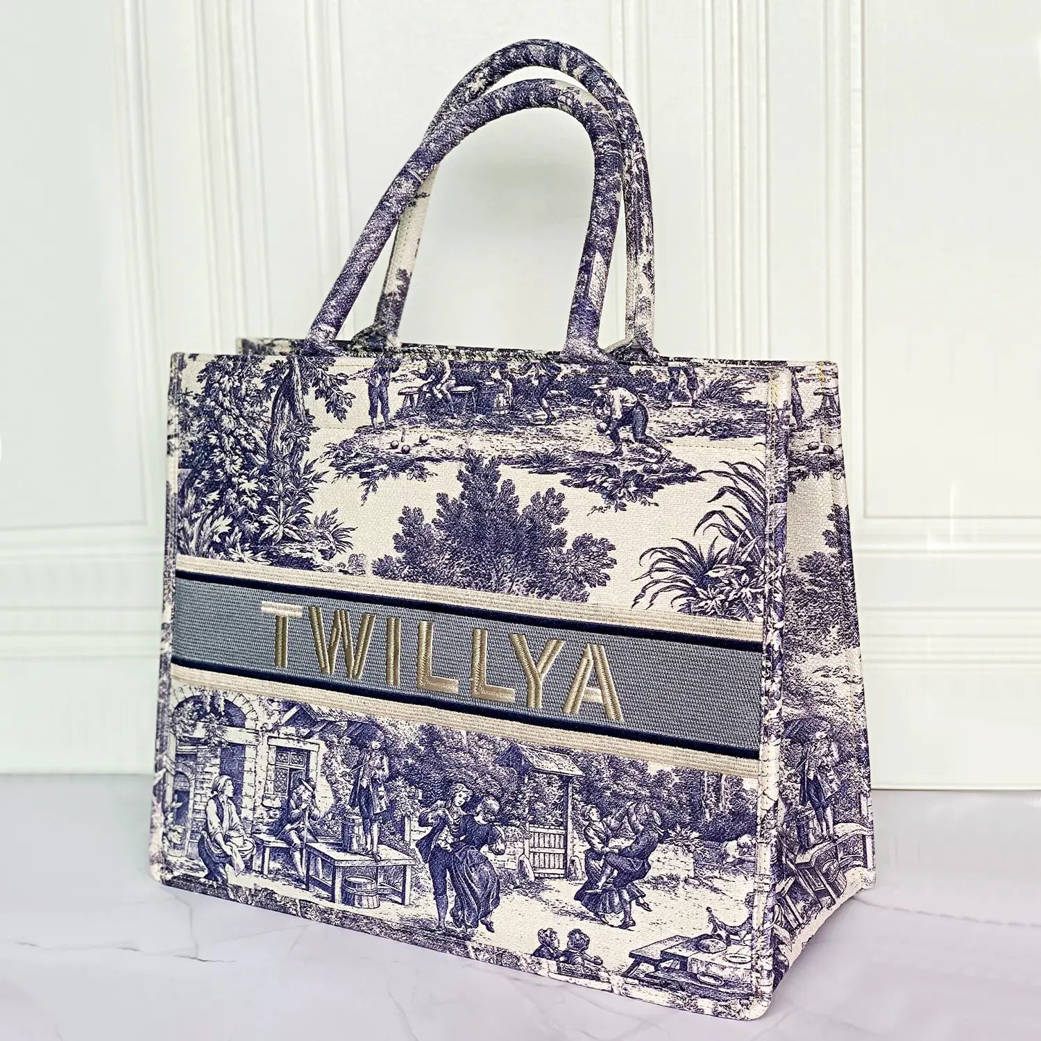 Structured personalized canvas book tote with embroidered name and blue Toile de Jouy countryside illustrations.