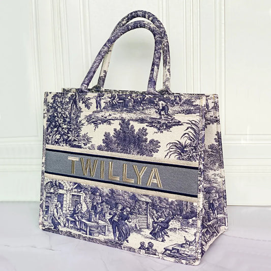Structured personalized canvas book tote with embroidered name and blue Toile de Jouy countryside illustrations.