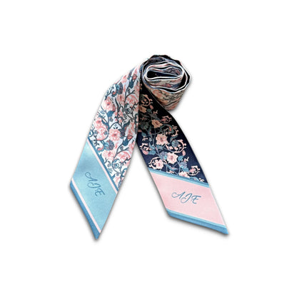 Two pointed ends of a personalised floral twilly scarf featuring the initials AJE, with pastel pink and turquoise colour-blocked tips and delicate vintage floral patterns.