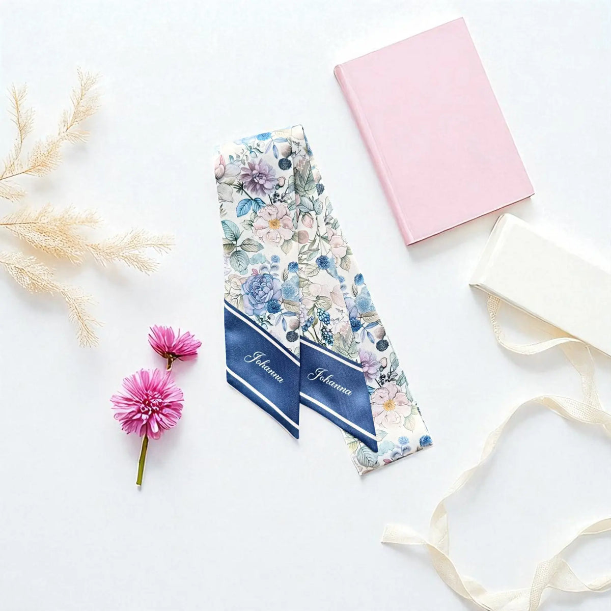 Close-up of a personalised floral twilly scarf with the name Johanna printed in elegant white script on navy blue pointed ends, complemented by delicate pastel botanical illustrations.