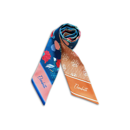 Two pointed ends of a personalised satin twilly scarf featuring the name Elisabeth, one with a pink border and blue floral pattern and the other with an orange border and tan geometric print.