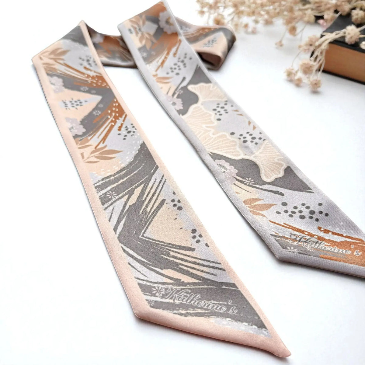 Custom name skinny scarf showcasing modern botanical artwork with peach blossoms, abstract leaf patterns, warm brown accents, and personalised lettering.
Foto 4