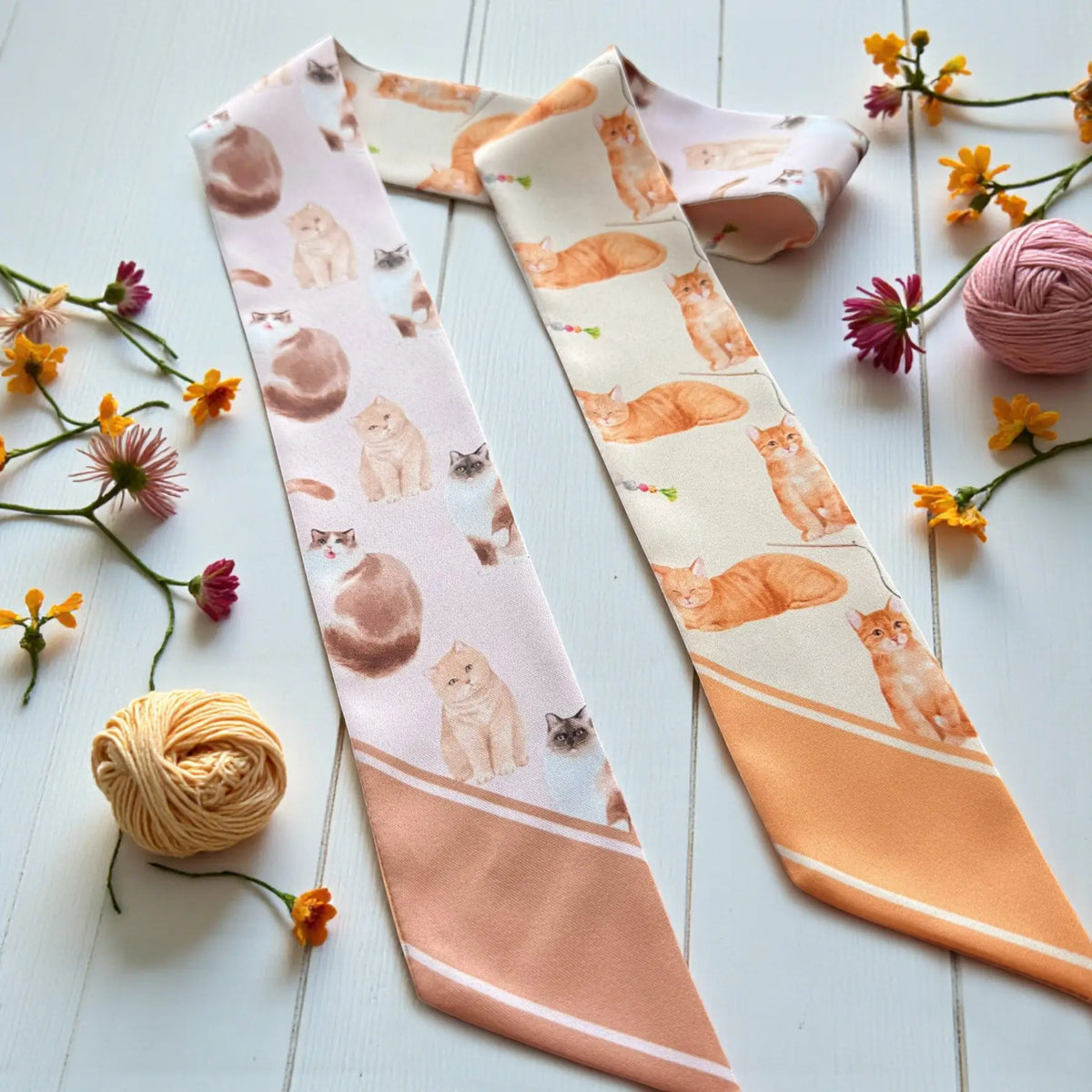 Cute cat pattern twilly scarf displayed with soft floral accents, featuring playful illustrated cats and peach ends.