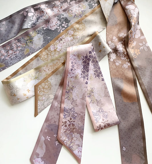 Elegant skinny twilly scarves featuring intricate vintage floral patterns, delicate blossoms, and geometric details in soft green, dusty pink, gray, and brown tones, arranged on a white background.