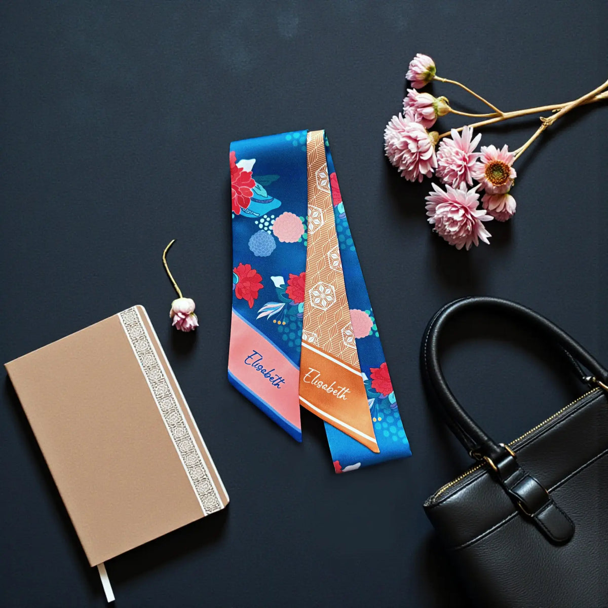 Elegant double-sided satin bag scarf combining a vibrant blue floral print with a warm tan geometric design, displayed flat against a dark background beside a brown leather handbag.