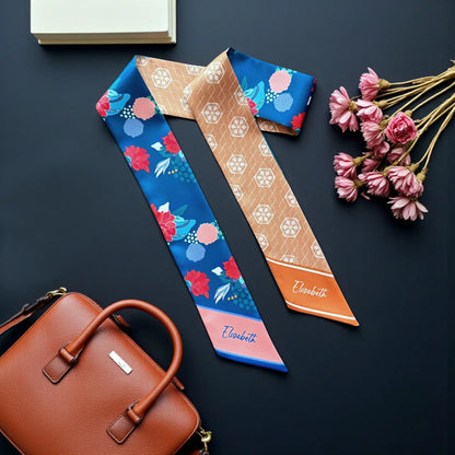 Double-sided satin twilly scarf featuring vibrant red and pink floral motifs on a deep blue background, contrasted with intricate tan geometric patterns and personalised name details.