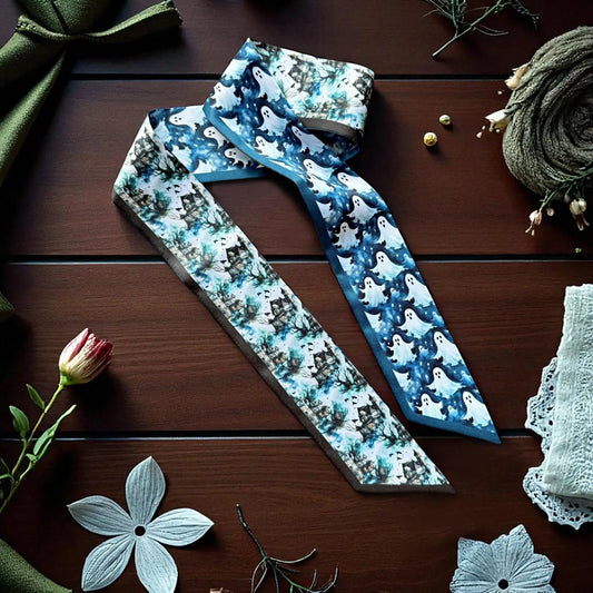 Blue Halloween twilly scarf featuring cute white ghosts, haunted houses, and spooky woodland illustrations, displayed on a dark wooden background.