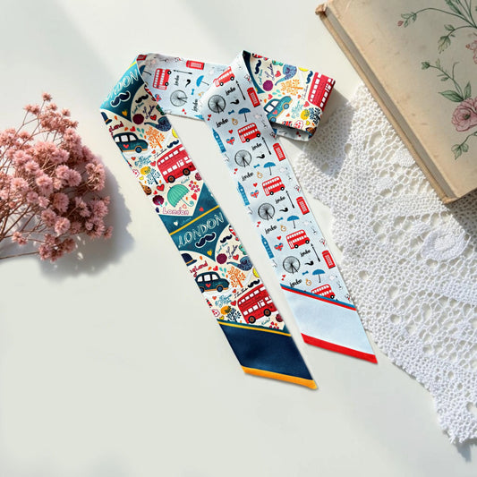 London-themed twilly scarf featuring red double-decker buses, Big Ben, the London Eye, and colorful British illustrations with navy blue and red accents.