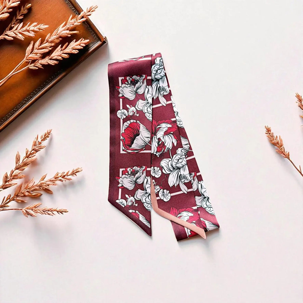 Maroon floral handbag scarf featuring detailed ivory and dusty pink blossoms, styled on a light background with dried flowers and warm brown accessories.