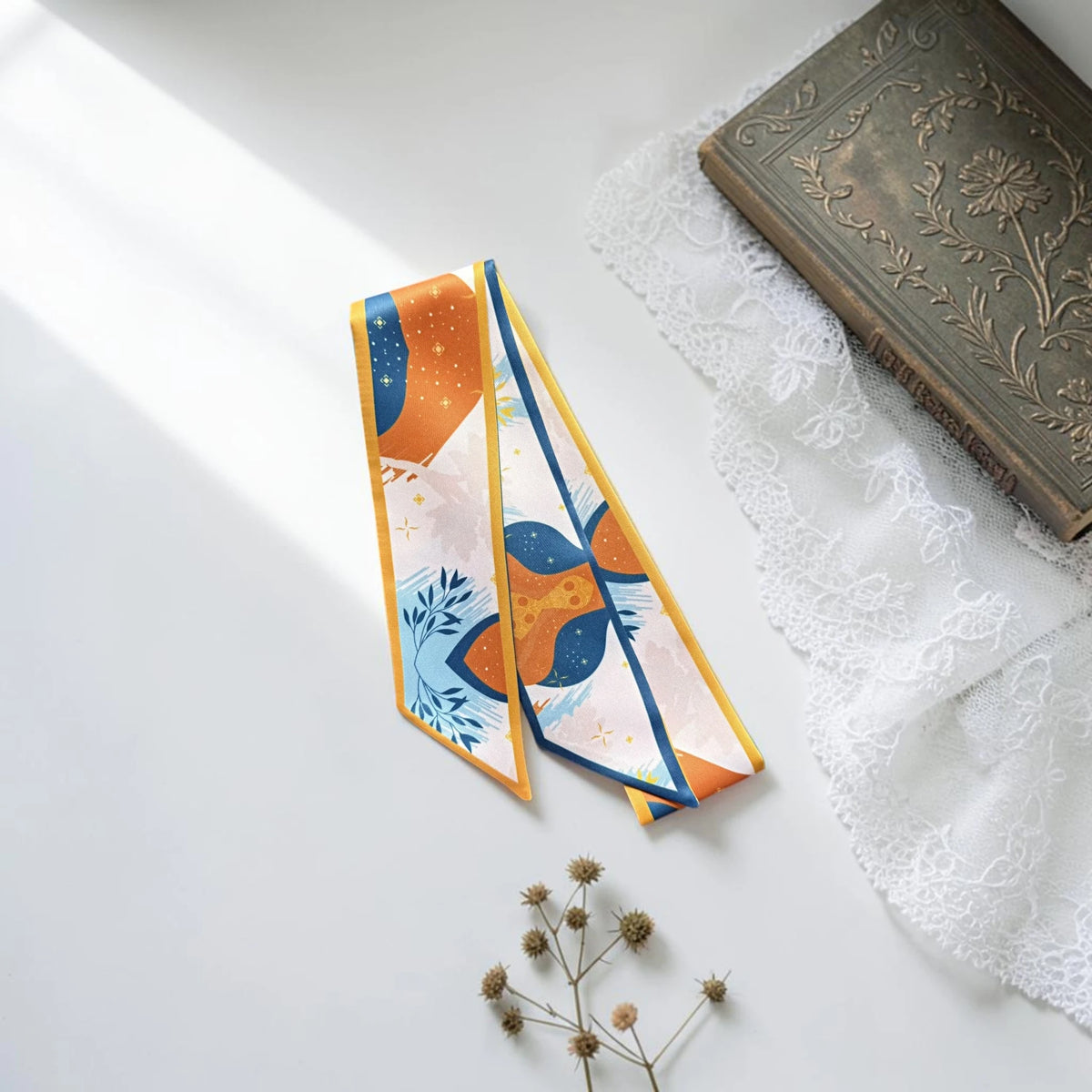 Elegant orange and blue bag handle scarf decorated with botanical leaves, playful geometric shapes, and subtle yellow floral accents.