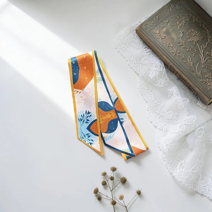 Elegant orange and blue bag handle scarf decorated with botanical leaves, playful geometric shapes, and subtle yellow floral accents.