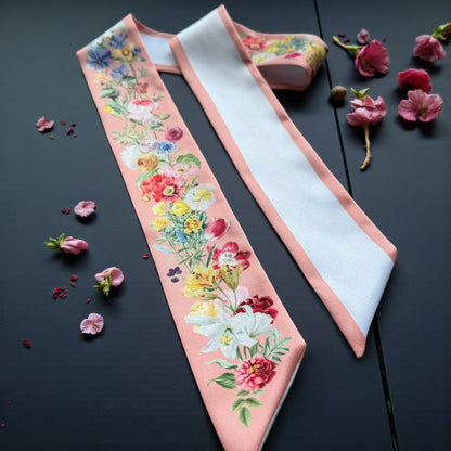 Elegant peach skinny scarf with vibrant floral illustrations and a contrasting white reverse side, displayed with delicate dried flowers.