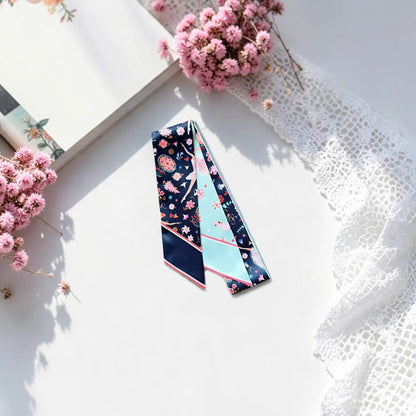Elegant ballet-themed twilly scarf featuring graceful ballerinas, romantic pink flowers, and whimsical decorative motifs, styled with dried pink flowers and white lace.