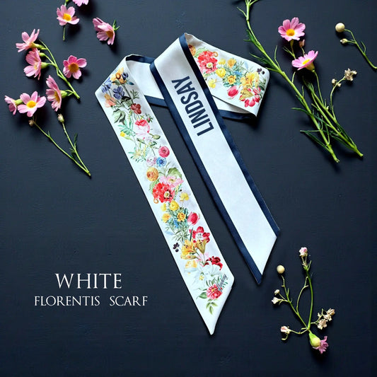 Personalised white twilly scarf featuring colourful watercolour wildflowers, navy blue trim, and custom name Lindsay, displayed on a dark background.