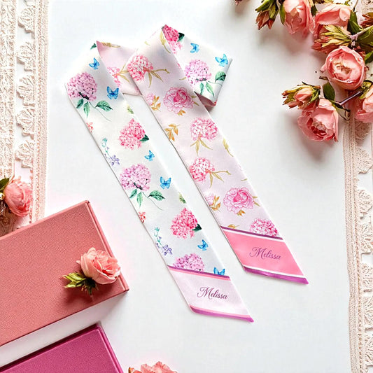 Personalized pink hydrangea twilly scarf featuring delicate floral patterns, blue butterflies, and custom name Melissa on pointed ends.