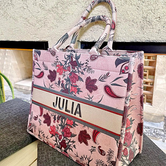 A soft pink book tote bag with a floral pattern, a custom name 'Julia' embroidered on the front.