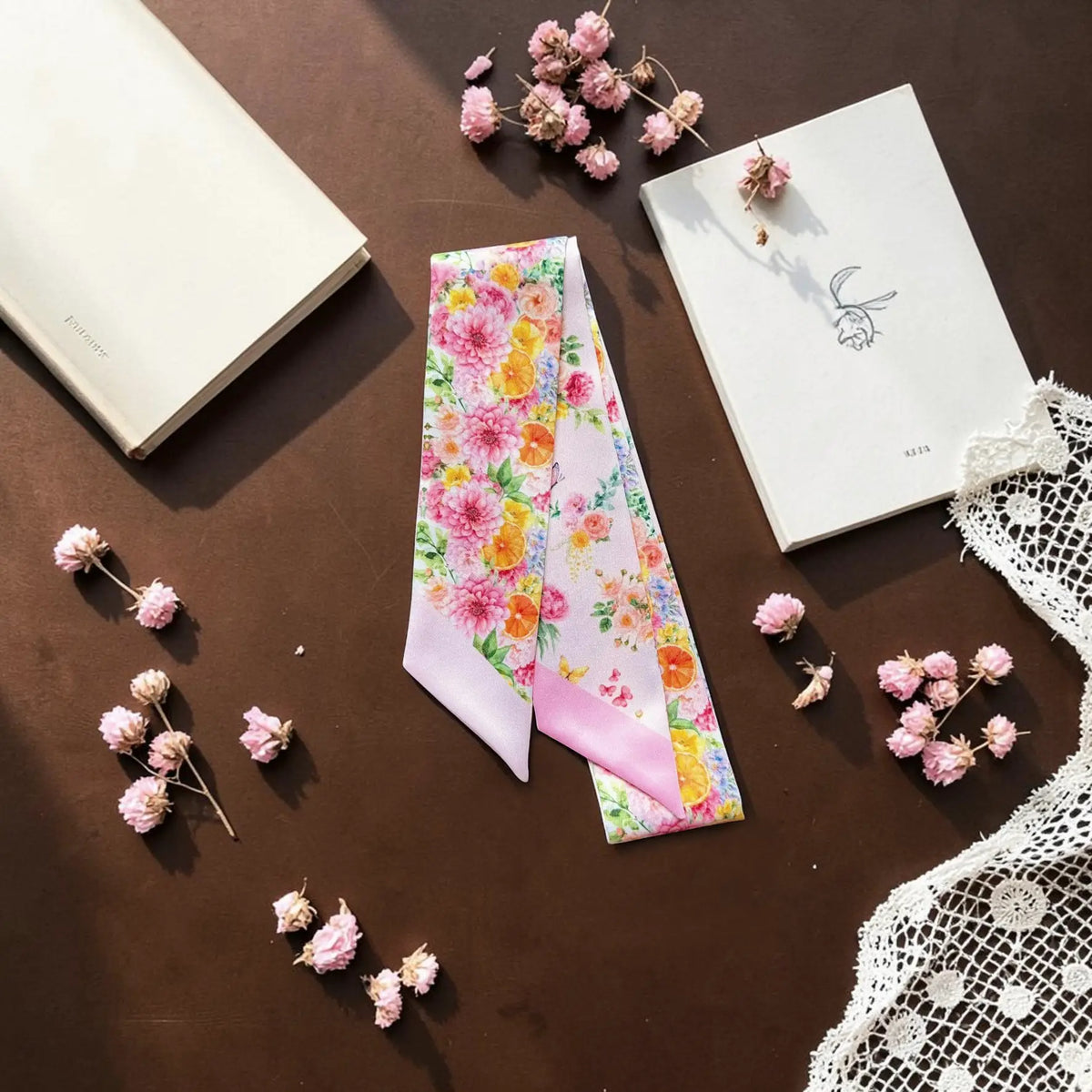 Pink botanical floral twilly scarf displayed with books, flowers and decorative accessories