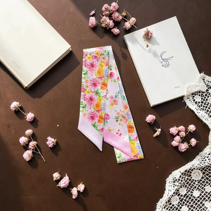 Pink botanical floral twilly scarf displayed with books, flowers and decorative accessories