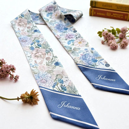 Floral satin bag scarf featuring a romantic English garden-inspired pattern with pastel roses, delicate wildflowers, and muted green leaves, accented by deep navy blue tips.