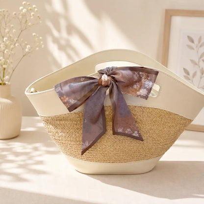 Elegant taupe floral handbag scarf styled into a decorative bow, featuring soft botanical illustrations and pointed ends against a neutral quilted bag.