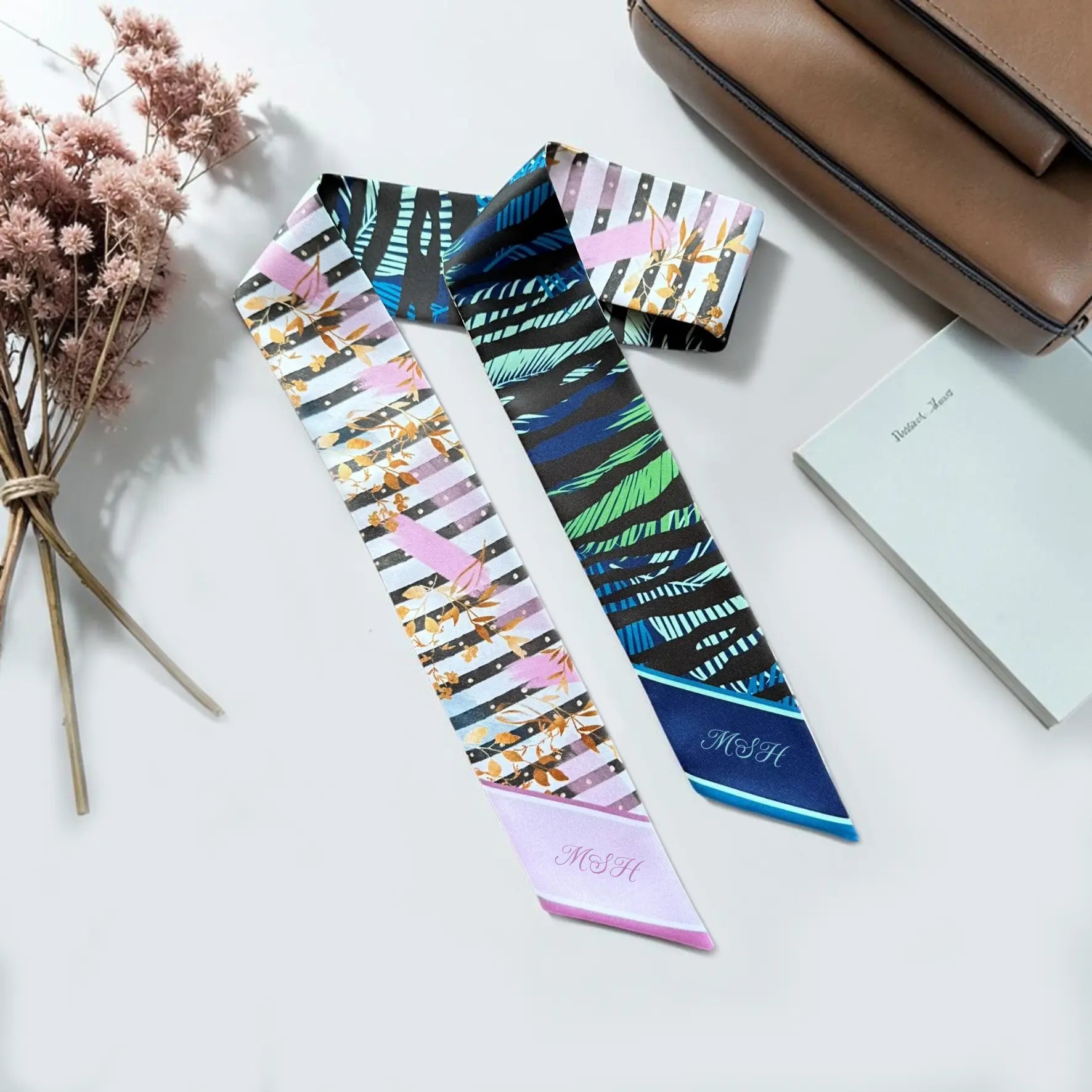Skinny scarves featuring abstract botanical leaf designs in pink, gold, navy, blue, and green.