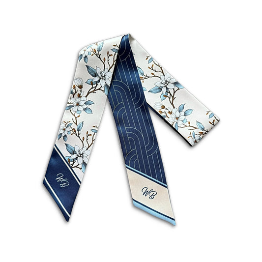 A monogrammed silk necktie featuring a navy blue and white floral pattern with abstract geometric designs, displayed on a clean white background.