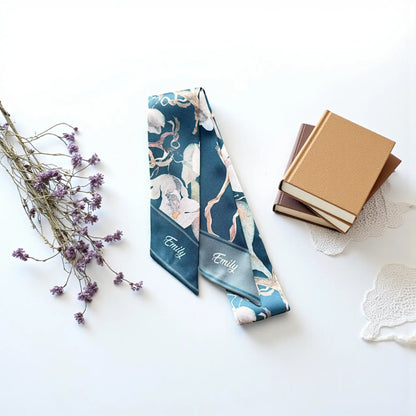 Close-up of a personalized floral scarf featuring the name Emily in white cursive lettering on deep teal and muted gray pointed ends.