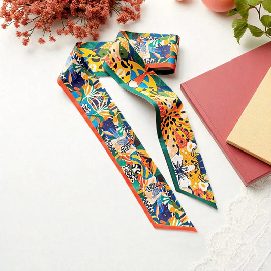 Colorful satin twilly scarf featuring a vibrant tropical jungle print with exotic foliage, abstract flowers, and playful animal-inspired patterns in orange, green, yellow, and blue.