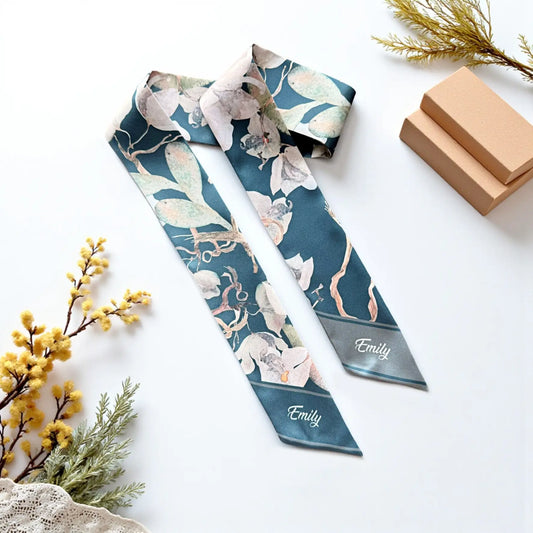 Personalized deep teal skinny scarf featuring soft ivory magnolia-like flowers, sage green leaves, delicate branches, and the custom name Emily on both pointed ends.