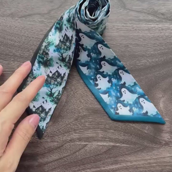 Halloween-inspired twilly scarf showcasing playful white ghosts, haunted houses, spooky trees, and intricate blue woodland patterns. A versatile skinny scarf for handbags, hair styling, and Halloween outfits.