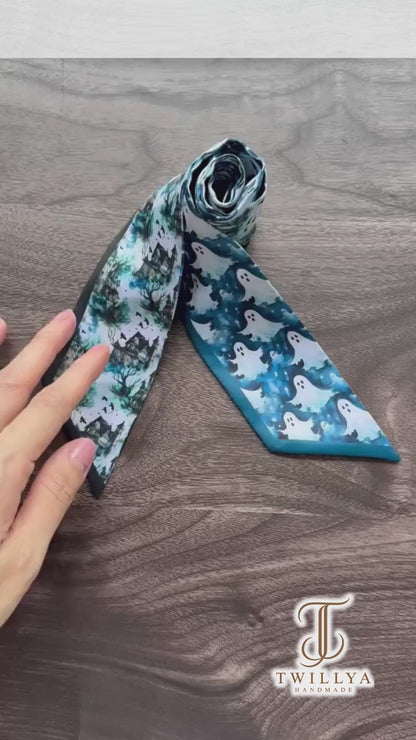 Halloween-inspired twilly scarf showcasing playful white ghosts, haunted houses, spooky trees, and intricate blue woodland patterns. A versatile skinny scarf for handbags, hair styling, and Halloween outfits.