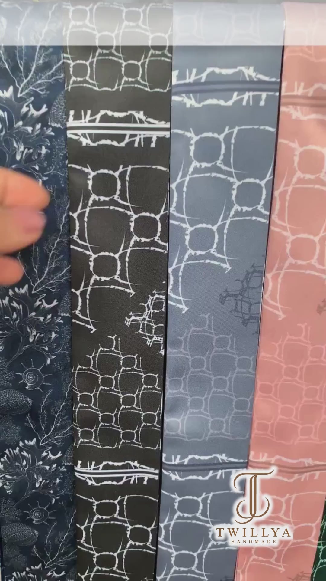 Video showcasing the Alba monochrome twilly scarf collection featuring elegant geometric patterns, bold stripes, and abstract motifs in black, brownish maroon, nude, blue, and green.