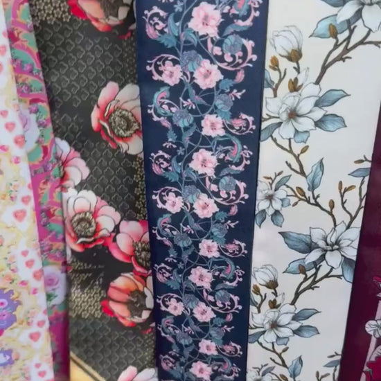 Personalised double-sided satin twilly scarf featuring intricate vintage floral patterns in navy blue and ivory, decorated with delicate pink blossoms and blue-green botanical vines. The scarf has contrasting pastel pink and turquoise pointed ends with custom initials AJE, making it an elegant accessory for handbags, hair styling, or gifting.
