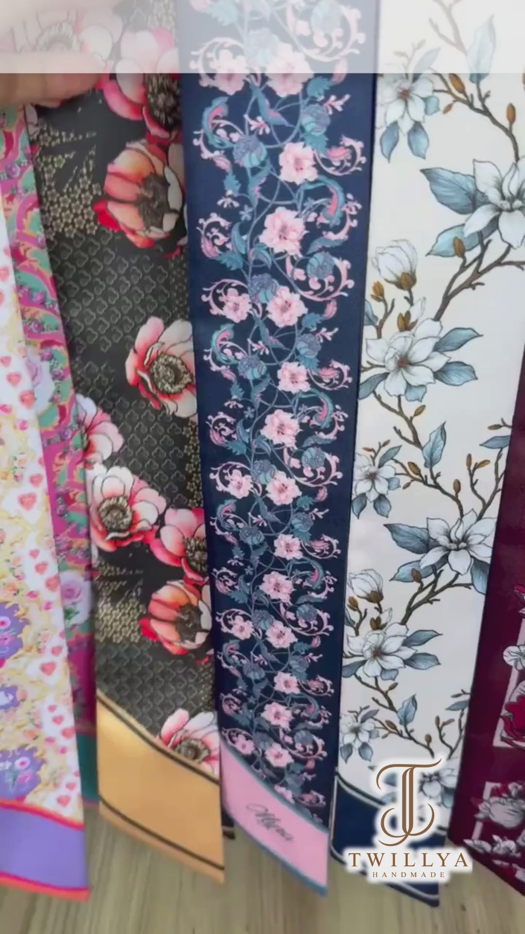 Personalised double-sided satin twilly scarf featuring intricate vintage floral patterns in navy blue and ivory, decorated with delicate pink blossoms and blue-green botanical vines. The scarf has contrasting pastel pink and turquoise pointed ends with custom initials AJE, making it an elegant accessory for handbags, hair styling, or gifting.
